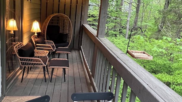 Eine Holzterrasse mit Lichterketten, Korbstühlen und Blick auf einen Wald.