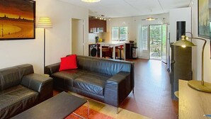 Een moderne woonkamer met een bank, een salontafel en een rood vloerkleed. Achtergrond toont een keuken met een eethoek.