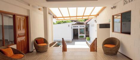 A spacious hallway with wicker chairs, a wooden door, and a view to a covered outdoor area.