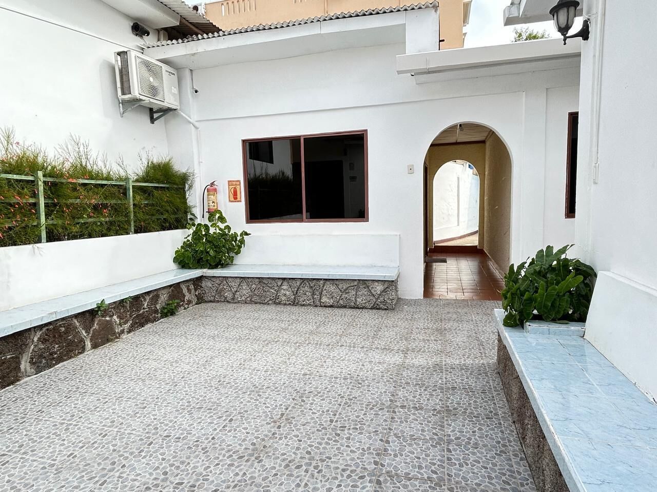 Un patio con piso de piedra, un banco y una pequeña zona ajardinada.
