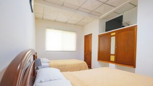 A hotel room with two beds, a wooden wardrobe, a television on the wall, and a window with blinds. - Hotel Mar Azul (Puerto Baquerizo Moreno)