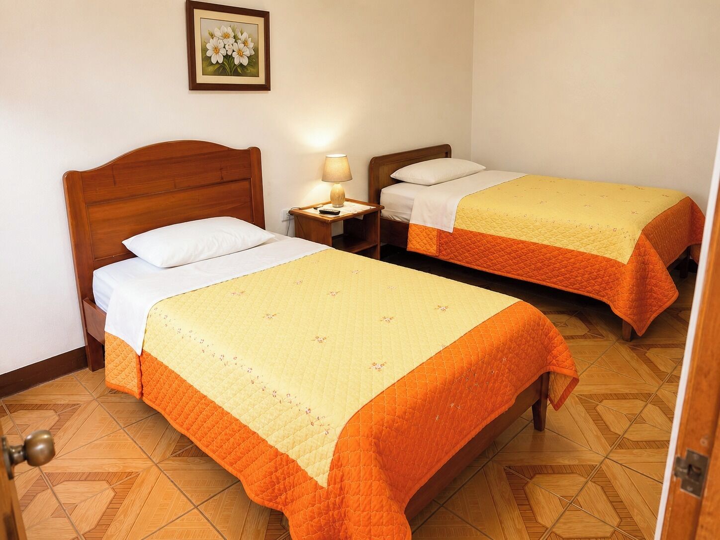 A hotel room with two single beds, a bedside table with a lamp, and a wooden floor.