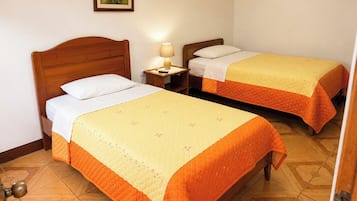 A hotel room with two single beds, a bedside table with a lamp, and a wooden floor.