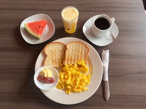 A breakfast plate with scrambled eggs, toast, butter, jam, a glass of orange juice, and a cup of coffee on a wooden table. - Hotel Mar Azul (Puerto Baquerizo Moreno)