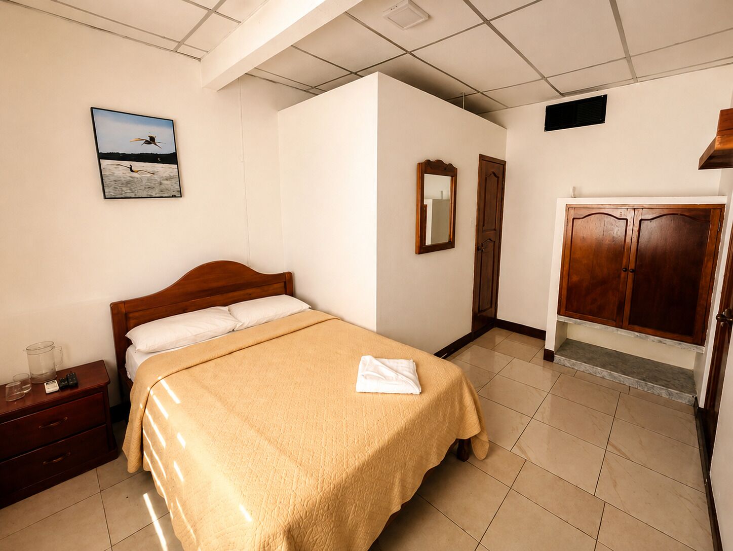A bedroom with a bed, a nightstand, a wardrobe, and a framed picture on the wall.