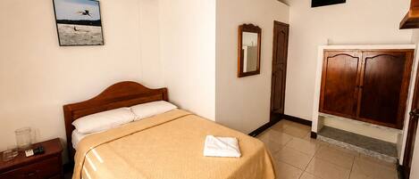 A bedroom with a bed, a nightstand, a wardrobe, and a framed picture on the wall.