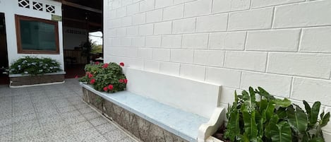 A courtyard with a white brick wall, a stone bench, and potted plants.