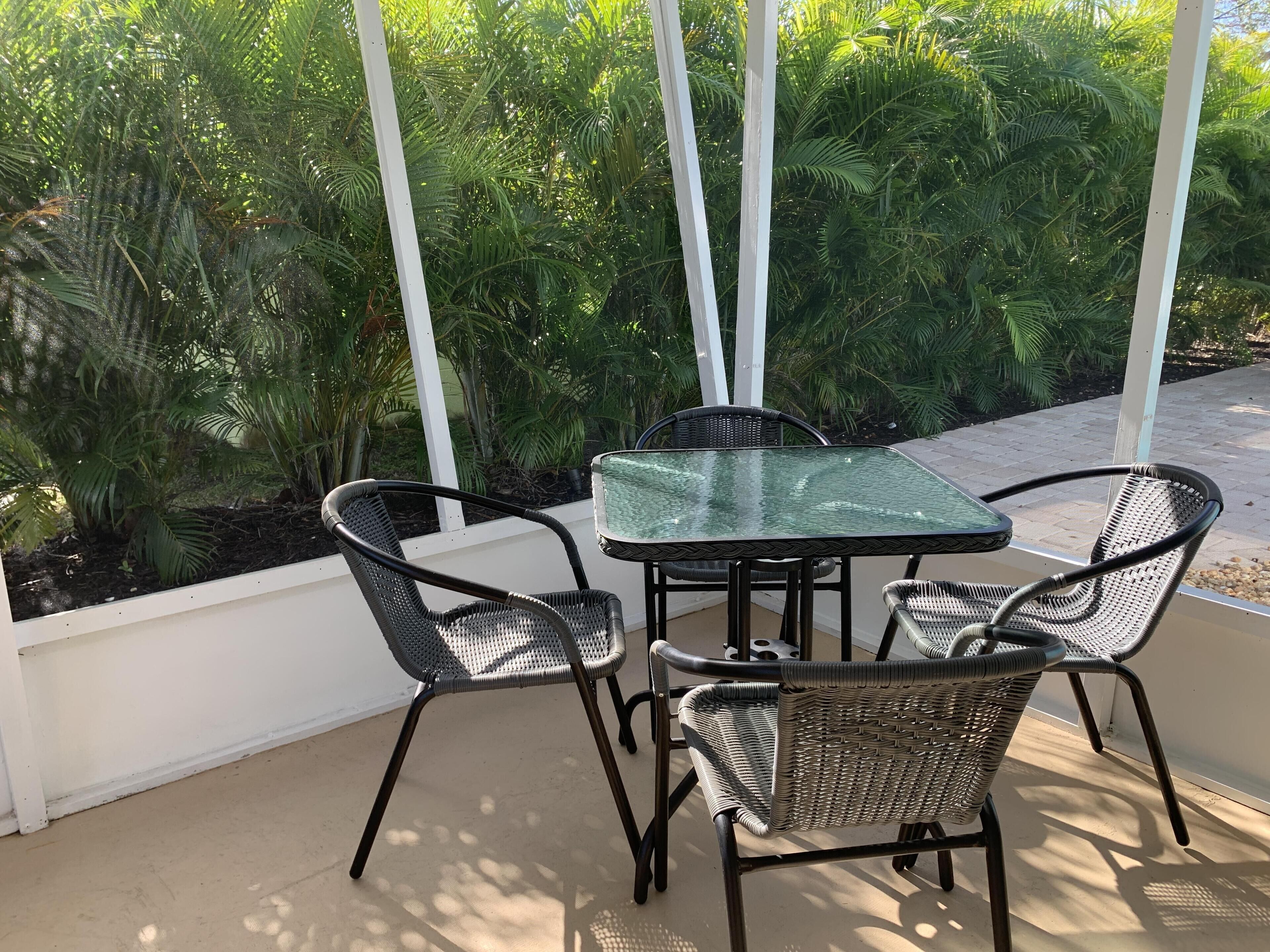 A glass-top table with four wicker chairs, surrounded by lush greenery.