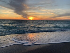 Ein Strand mit Wellen und einem Sonnenuntergang.