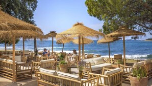 Un salón junto a la playa con sombrillas de paja, muebles de mimbre y plantas en macetas.