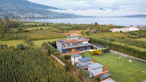 Une maison moderne dotée d’un grand balcon en verre, entourée d’une végétation luxuriante et offrant une vue sur un lac.