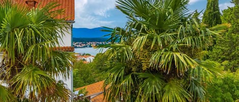 Vista costera con un edificio de techo rojo y tejas, rodeado de vegetación exuberante y palmeras.