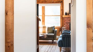 A wooden interior hallway leading to a living area with a sofa and chairs, a sign above the door, and a light fixture on the wall.