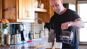 A man pouring coffee into two cups on a wooden kitchen island.