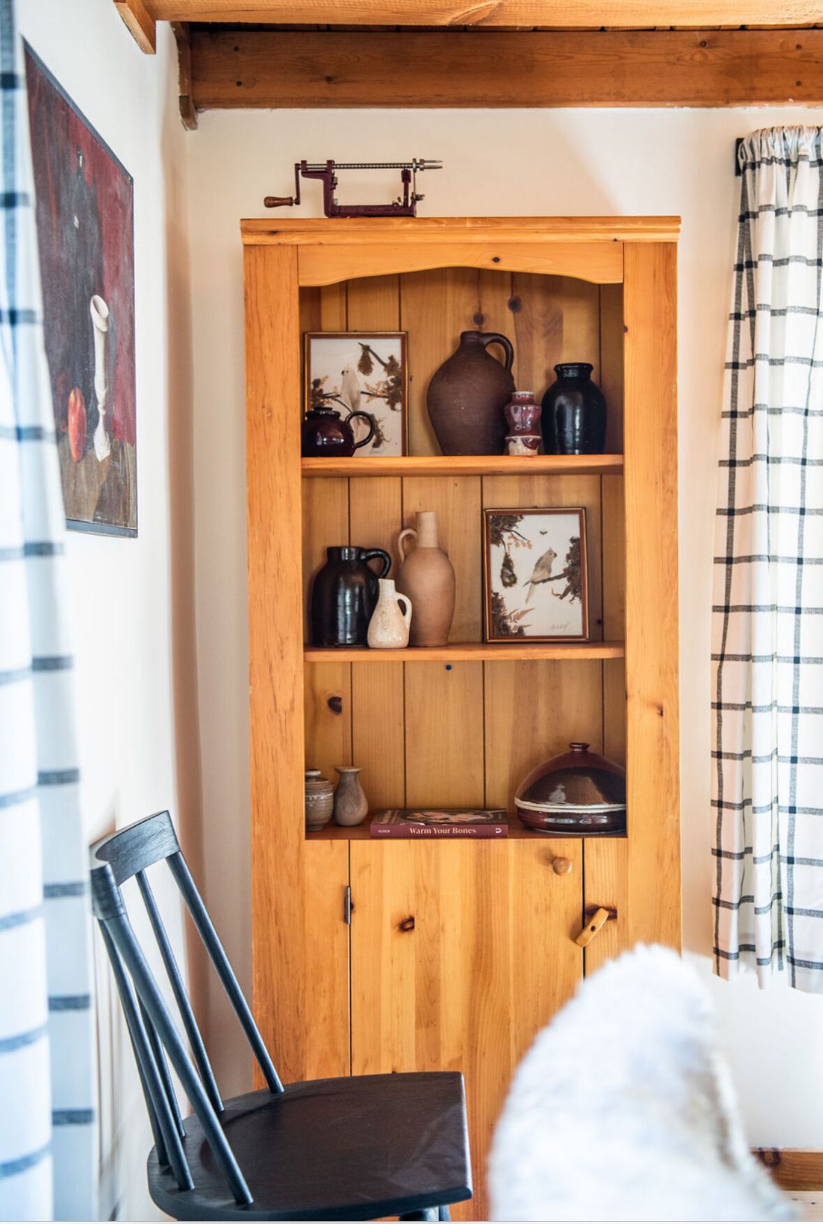 A wooden cabinet with shelves holding various pottery and framed pictures.