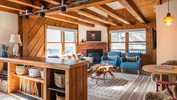 A rustic interior with exposed wooden beams, a brick fireplace, and a cozy seating area with blue-striped sofas.