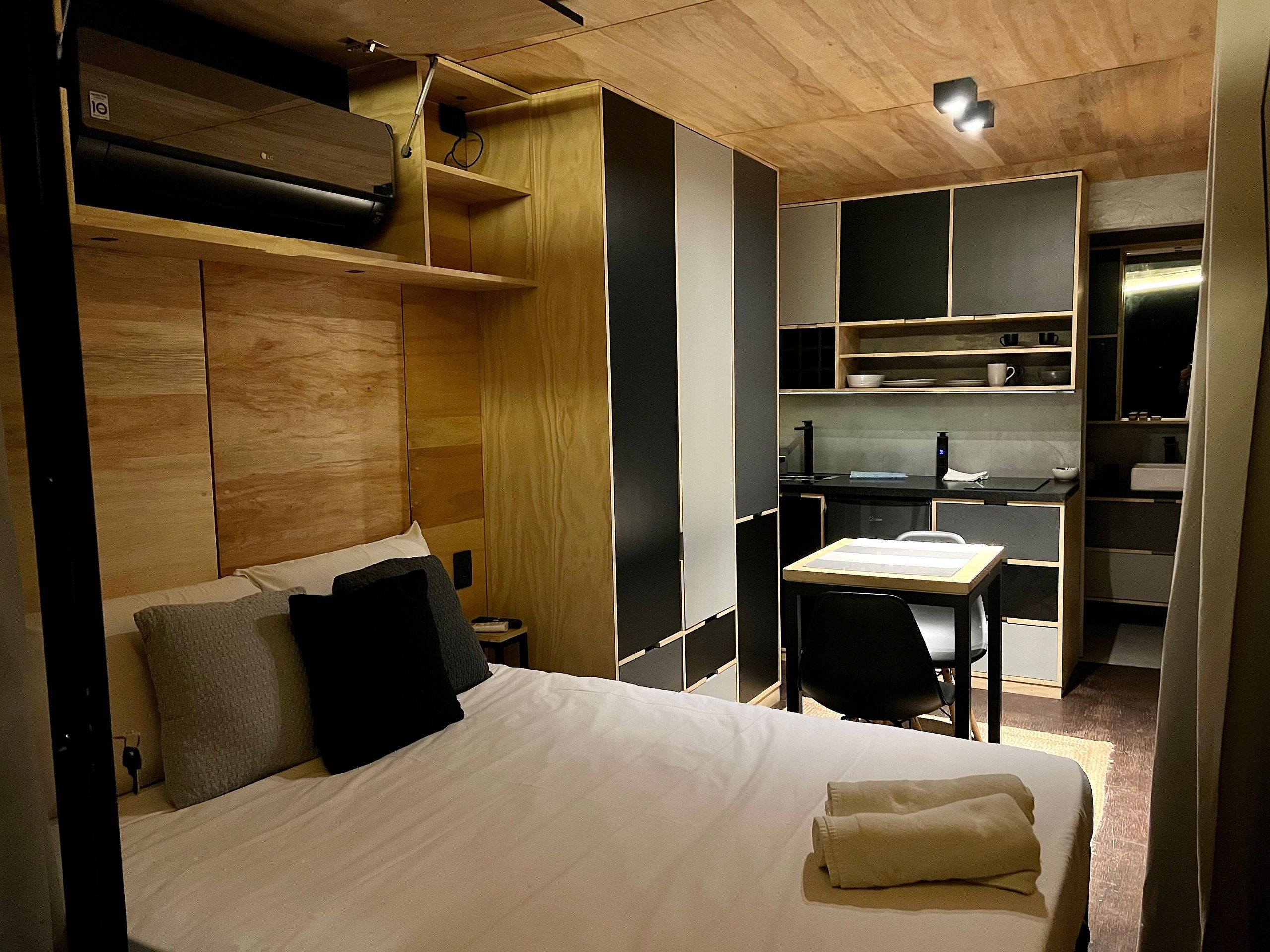 A compact hotel room with a bed, a desk, and a kitchenette.