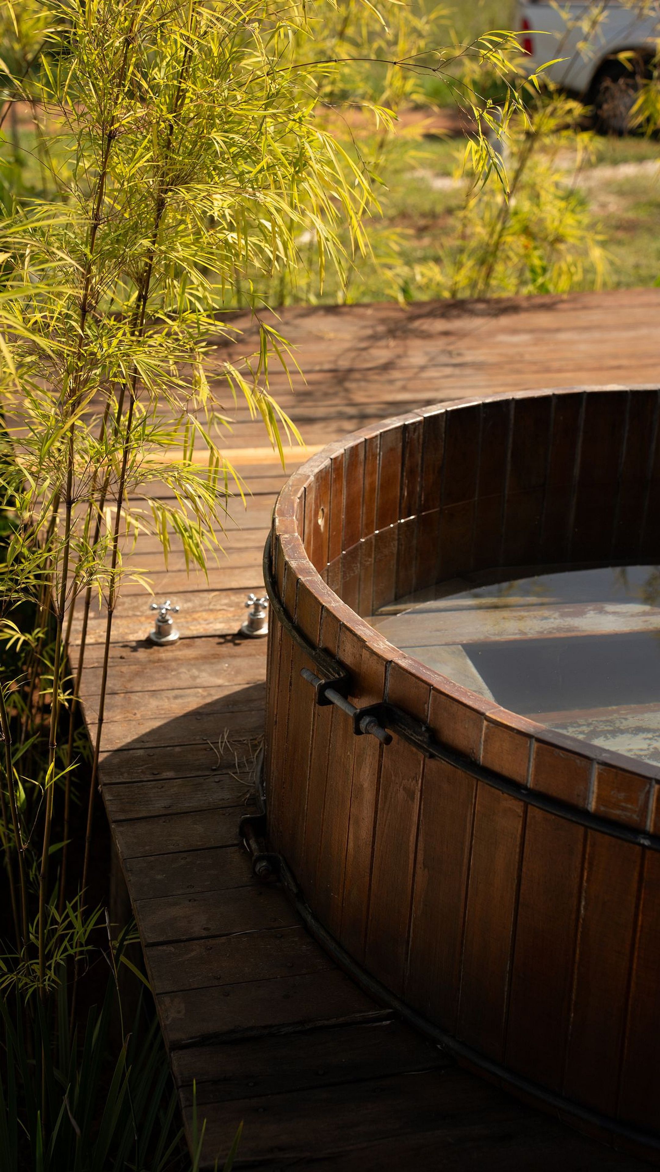 A hot tub with a wooden exterior, surrounded by a wooden deck and bamboo plants.