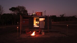 A small, open-sided structure with a fire pit and seating area, surrounded by trees.
