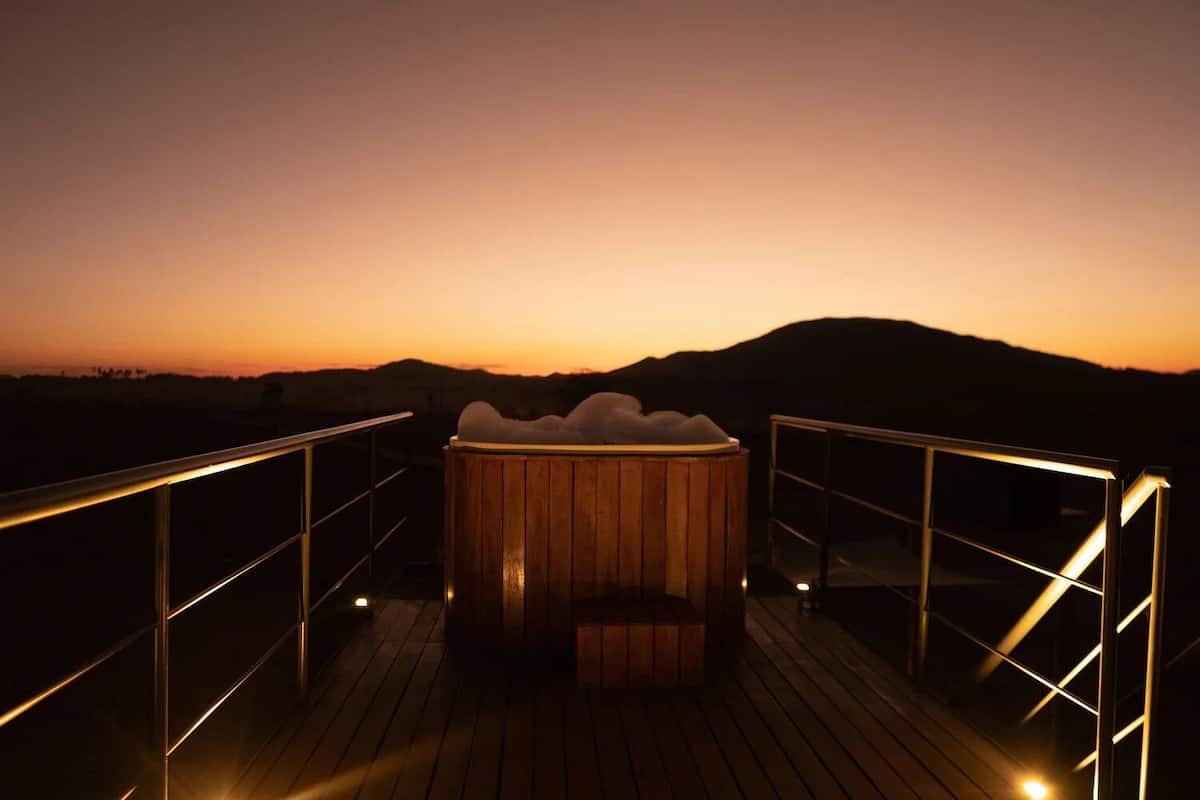 A wooden deck with a hot tub at sunset.