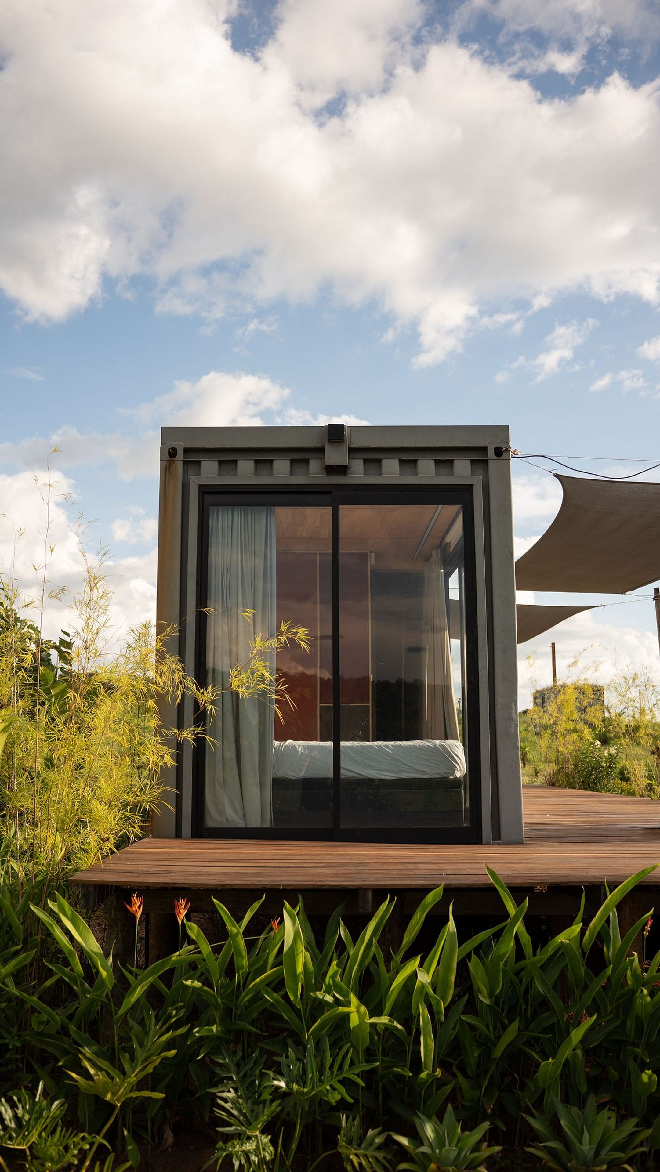 Un espacio exterior moderno y cerrado con cama, ventanas grandes y una terraza de madera.