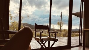 A room with a large window, a wooden chair, a wooden table, and a book on a table.