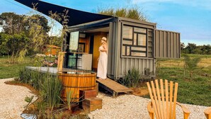 Een moderne, compacte hut met een houten terras en een klein zitje buiten.