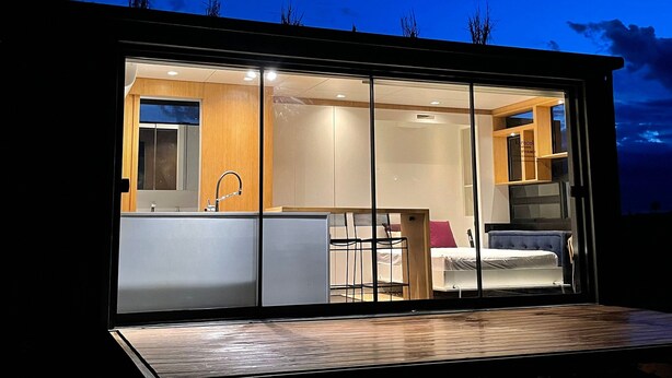 A modern, well-lit interior of a cabin with a visible kitchen area, a bed, and a bathroom.