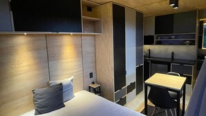 A modern hotel room with a bed, bedside table, and a small desk with a chair.