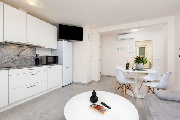 A modern kitchen with white cabinets, a black microwave, and a flat-screen TV.