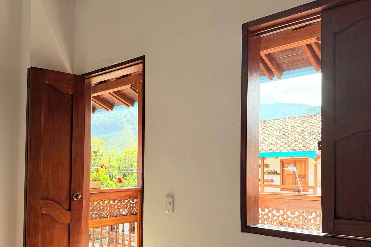 A room with a bed, a wooden door, and a window with a view of a building and greenery.