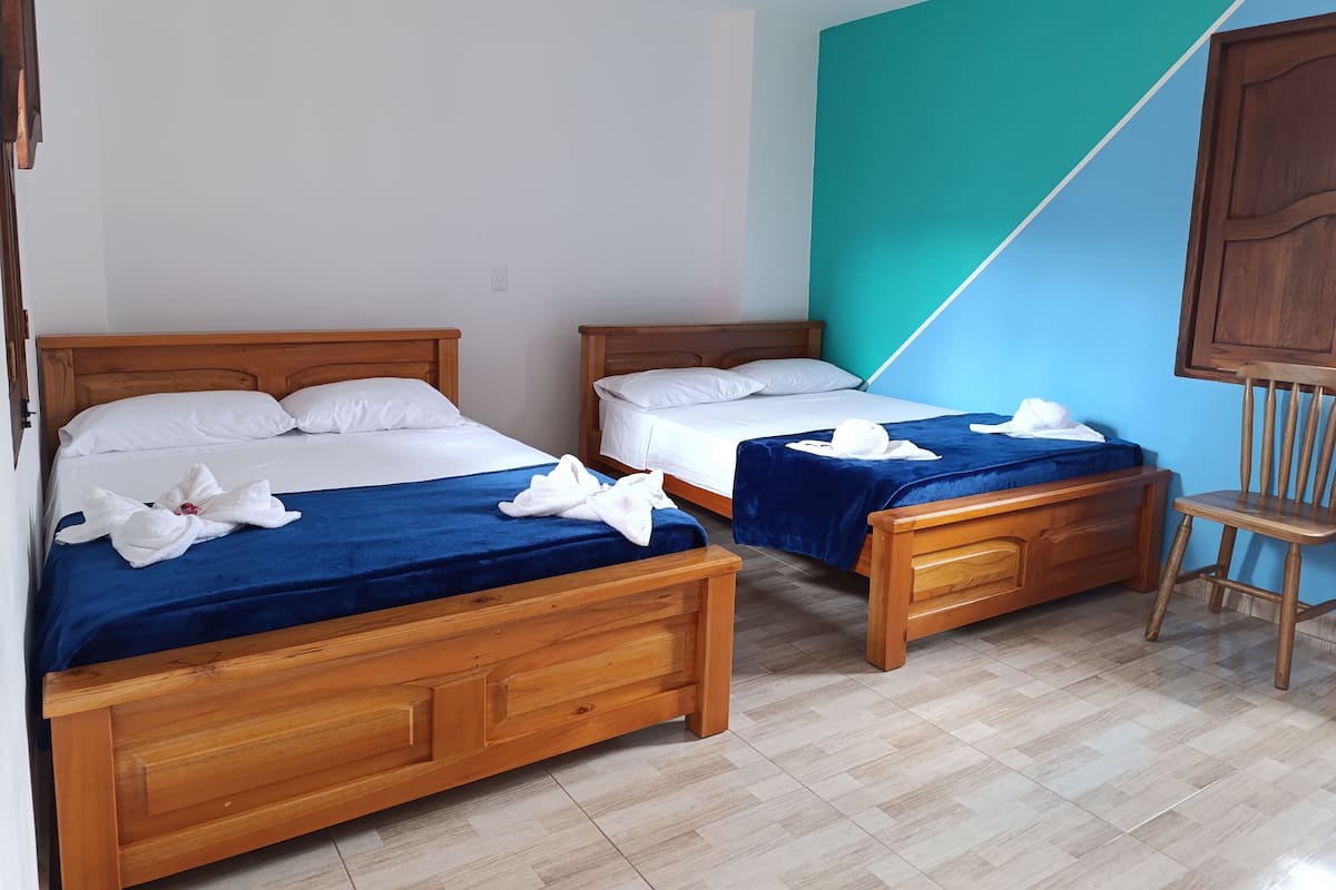 Two wooden beds with blue and white bedding, a wooden chair, and a teal accent wall.