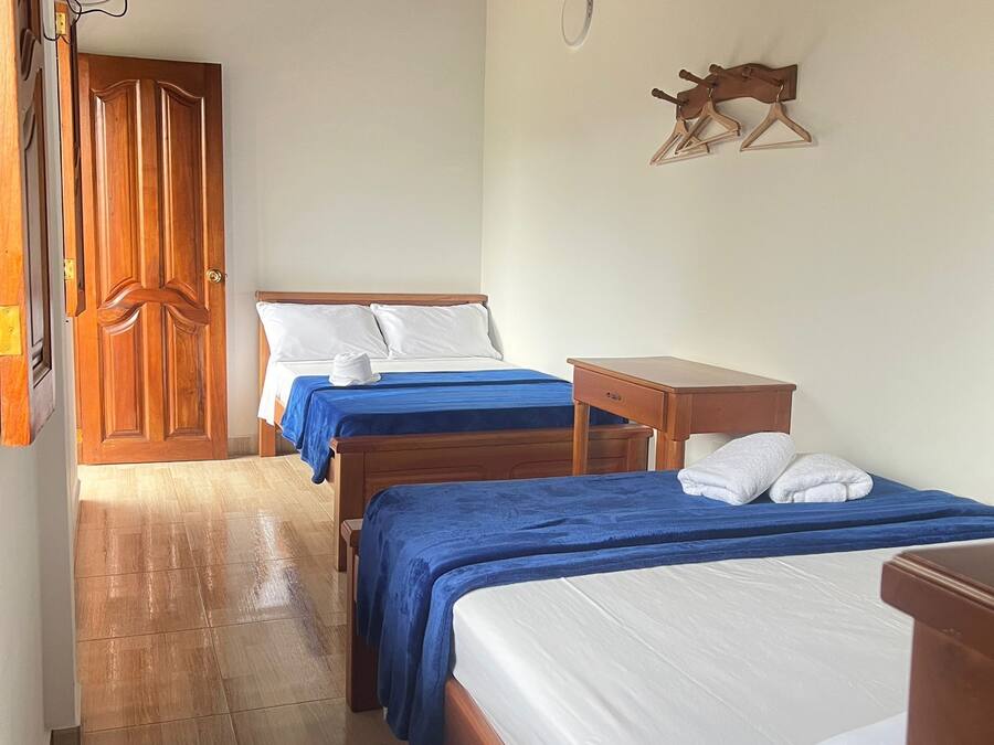 A hotel room with two beds, a wooden wardrobe, a small table, and a wall-mounted decoration.