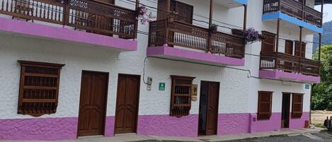 Un edificio de varios pisos con balcones, barandas de madera y una combinación de paredes blancas y moradas.