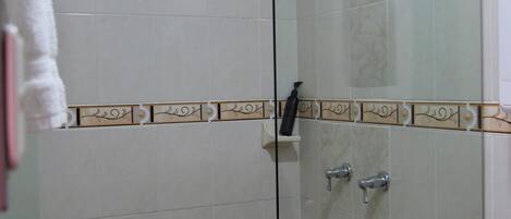 Ducha con cerramiento de vidrio, azulejos blancos y un borde decorativo.