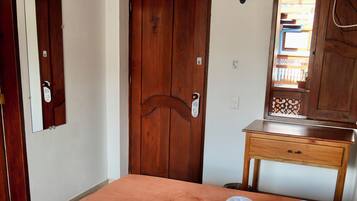 Une chambre d’hôtel avec un lit, une porte en bois, une petite table en bois et un ventilateur.