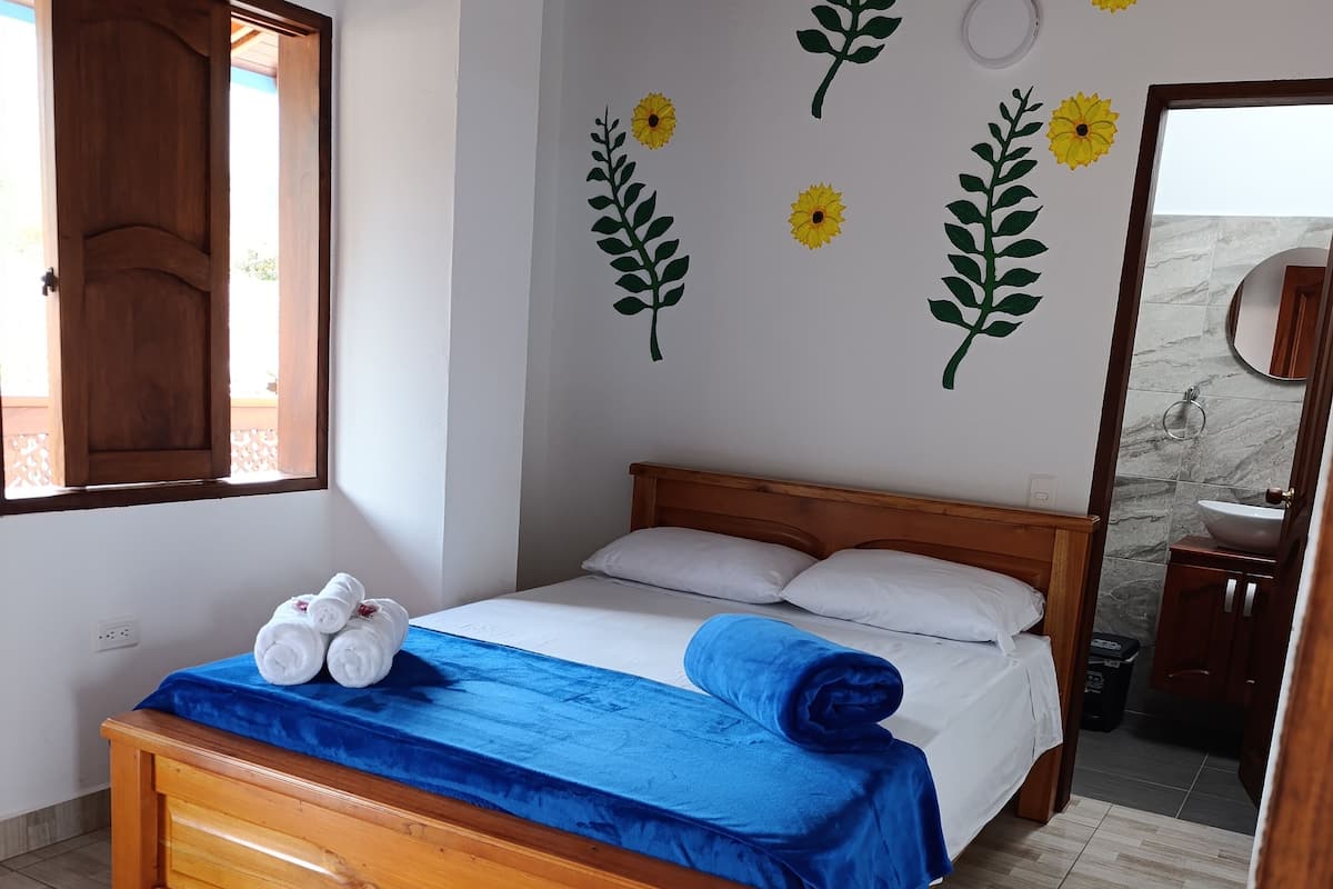 A bedroom with a wooden bed, a blue bedspread, and towels on the bed. There are wall decals of sunflowers and leaves.