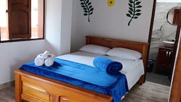 Un dormitorio con una cama de madera, una colcha azul y toallas sobre la cama. Se observan adhesivos murales con motivos de girasoles y hojas.