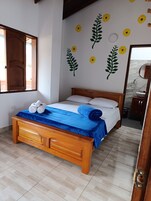 Un dormitorio con una cama de madera, una colcha azul y toallas sobre la cama. Se observan adhesivos murales con motivos de girasoles y hojas.