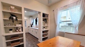 Una cocina moderna con armarios blancos, una mesa de madera y objetos decorativos en estantes.