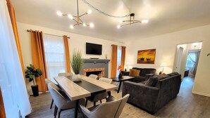 Una sala de estar moderna con comedor, chimenea y televisor montado en la pared.