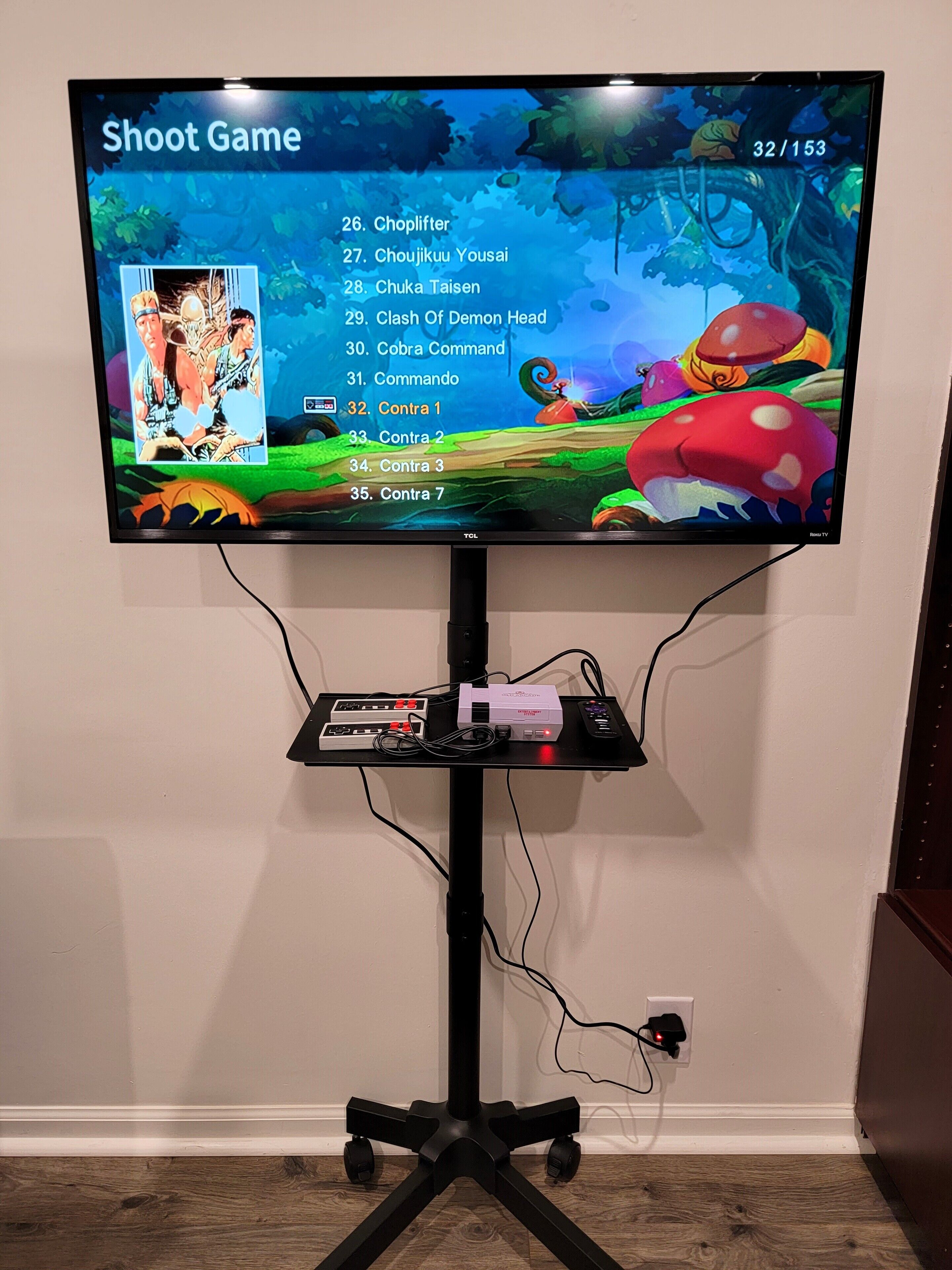 Un téléviseur fixé sur un support, avec un menu de jeu affiché à l’écran, une télécommande et un décodeur placés sur le support.