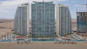 A modern hotel with a curved facade, multiple balconies, and a pool area with sun loungers.