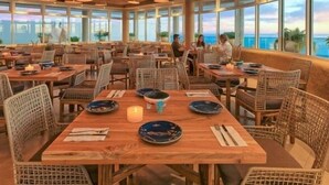 A spacious dining area with wicker furniture and large windows offering a view of the ocean.