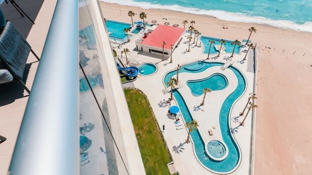 An aerial view of a resort with multiple swimming pools, a beach, and palm trees.