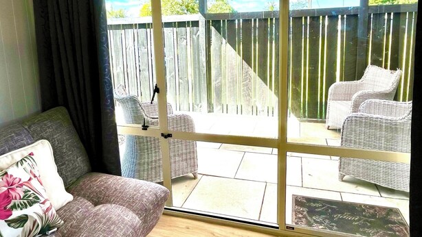 Une pièce dotée d’une porte-fenêtre coulissante donnant sur un patio extérieur aménagé avec des meubles en osier.