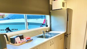Une cuisine de taille réduite, équipée d’un évier, d’un réfrigérateur et d’une fenêtre donnant sur un parking.