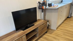 Une cuisine moderne avec un téléviseur encastré dans un meuble en bois, un sèche-cheveux posé sur un support, et un plan de travail doté d’un évier et de placards.