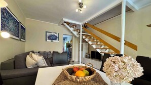 A living room with a sofa, a coffee table with fruit and flowers, a staircase, and a TV.