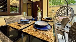 An outdoor dining area with wicker furniture, a hanging chair, and a table set with plates and glasses.